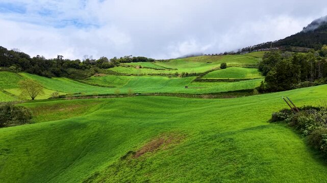 Cinematic panoramic view of the rolling green hills on Sao Miguel Island Azores Portugal showcasing vibrant pastureland patchwork fields and peaceful countryside beneath dramatic cloud filled skies