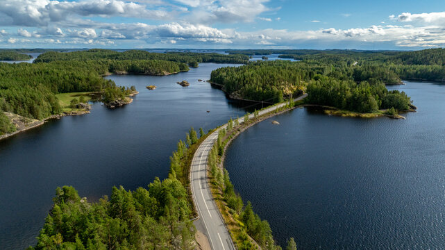 Finland - 26 June 2026: Aerial view of Saimaa lake with a road crossing the water, surrounded by lush green forests under a blue sky with scattered clouds.