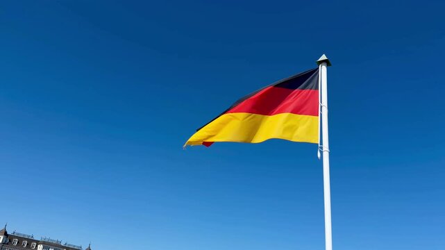The German flag flutters in the wind against a blue sky.