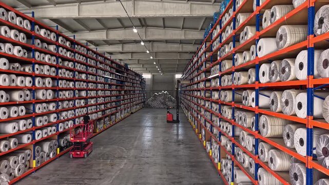 Yarn bobbins are stored on high shelves inside a textile warehouse with forklift operation. This video frame shows stock management, raw material storage, logistics, and industrial warehouse layout.