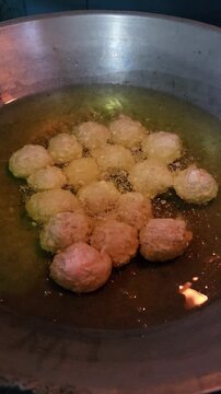 Deep frying savory golden meatballs in hot bubbling oil inside a traditional metal wok