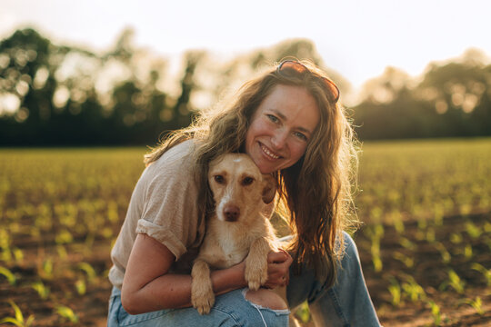 Woman embracing small dog in field at sunset
