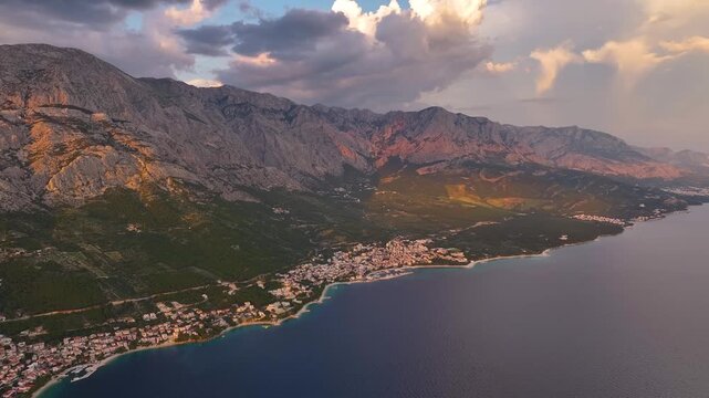 Breathtaking aerial view of Brela coastline and mountains in Croatia at sunset with water and buildings along the shore