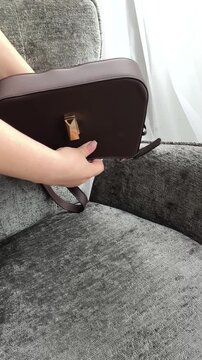 Woman shaking handbag and spilling personal items onto chair, looking for something inside bag, organization and daily life concept.