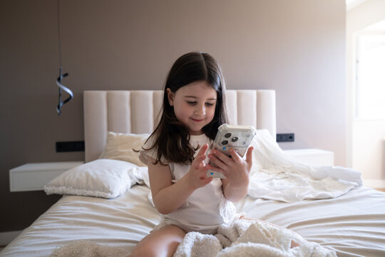 Child sitting on bed at home using a smartphone