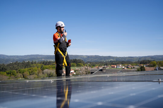 Technician using walkie talkie near solar panel on rooftop