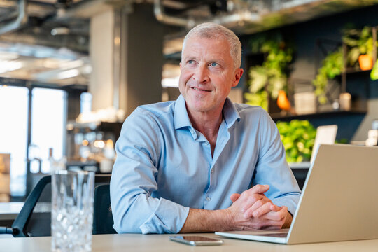 Smiling executive thinking at office desk with laptop