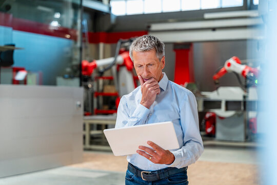Thoughtful engineer holding tablet in modern factory