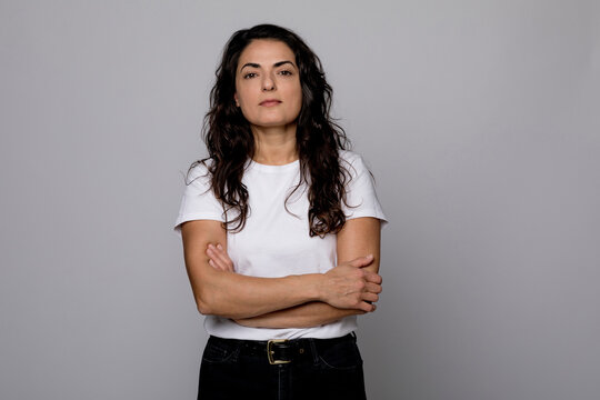 Confident woman standing with arms crossed against gray background