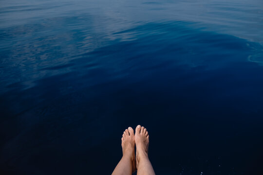 Point of view of bare feet dangling over calm blue sea water