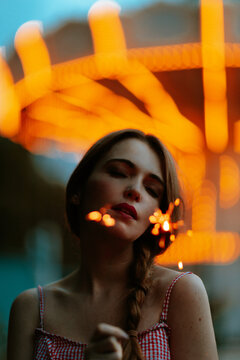 Holding a glowing sparkler at an amusement park at night