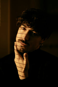 Indoor portrait of a young man with serious expression and dramatic shadows on face