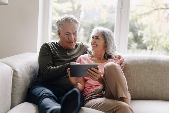 Happy senior couple relaxing on couch at home using tablet