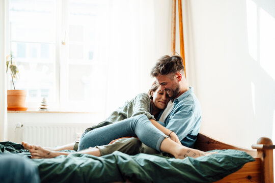 Happy couple embracing while sitting on bed at home
