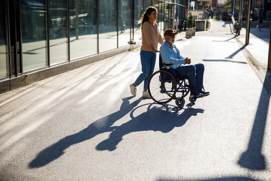 Volunteer pushing man in wheelchair on footpath with shadow