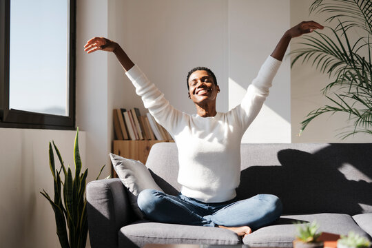 Smiling relaxed woman sitting on couch at home with closed eyes