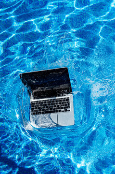 High angle view of laptop falling in swimming pool