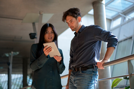 Multiracial business colleagues discussing over tablet PC in corridor