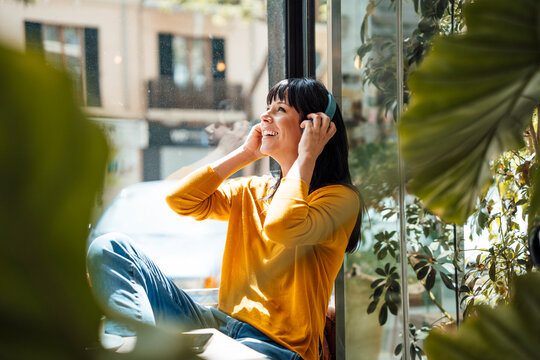 Happy mature woman wearing wireless headphones listening to music