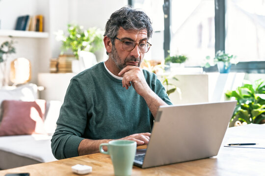Adult freelancer thinking while working on laptop at desk