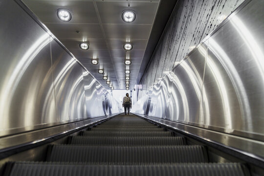 Back view of woman standing on escalator of underground station