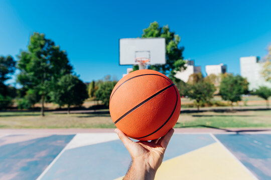 Man holding basketball at court on sunny day