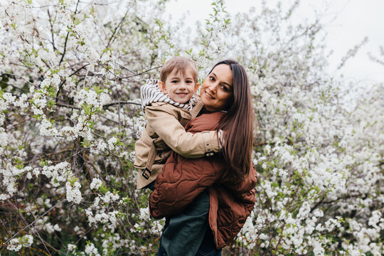 Mother holding son outdoors near blooming spring tree
