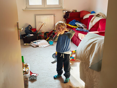 Little boy standing in his messy room building cross with his fingers