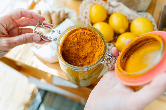 Hands of woman with turmeric jar at table