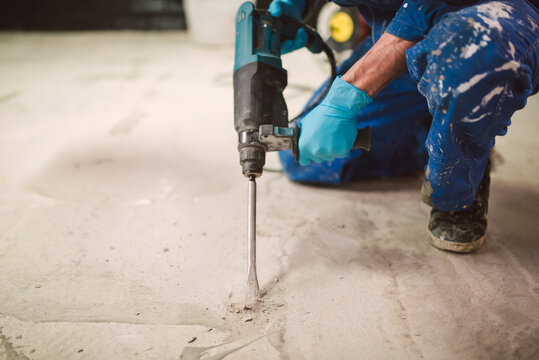 Bricklayer removing irregularities on floor screed with jackhammer