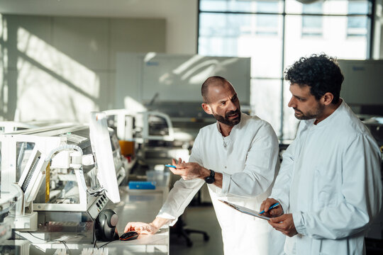 Scientists in lab coats discussing research data at a monitor