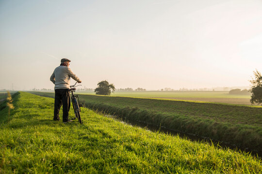 Senior man in rural landscape pushing bicycle