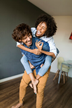 Cheerful man carrying girlfriend piggyback at home