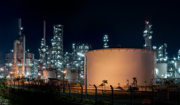 Industrial Nightscape: A sprawling oil refinery complex is illuminated against the night sky, showcasing the intricate network of pipes, towers, and storage tanks under the glow of artificial lights.