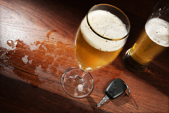 Two beer glasses and a car key on the dark wooden bar in a pub, concept against dangerous driving after alcohol consumption, copy space