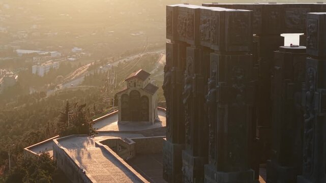 Drone shot revealing the sunrise at the Annunciation Church framed through the columns of the Chronicle of Georgia monument with warm morning light.