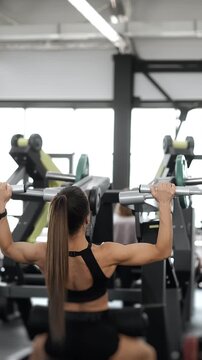 Fit athletic woman performing shoulder press on a plate loaded machine in a modern fitness gym. Strength training focused on shoulders, upper body and healthy lifestyle.