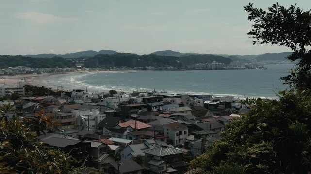 Scenic view over Kamakura, Japan, showing coastal rooftops, sandy beach, ocean bay, gentle waves, and green hills. Ideal for travel, seaside lifestyle, tourism, and Japanese town concepts.