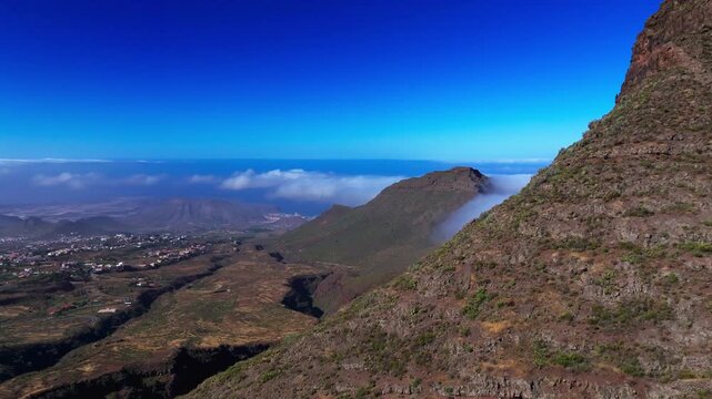 Aerial view of volcanic mountain slopes with drifting clouds and distant villages
