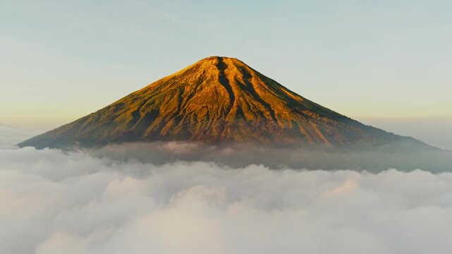 Aerial view of Mount Sindoro rising above a thick layer of clouds during golden hour in Kecamatan Kedu, Jawa Tengah, Indonesia.