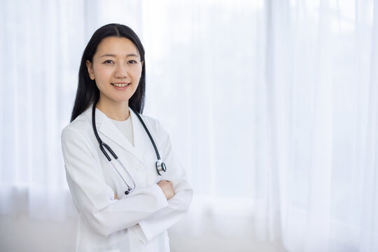 Young Japanese female doctor arms crossed smiling at camera by window