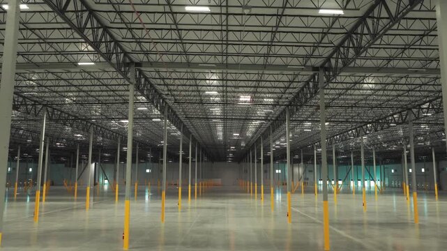 Wide tilting down aerial shot inside a large vacant distribution warehouse. 4K