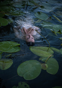 Mystical Slavic mermaid floating in deep lake water among green water lilies, pagan nymph undine in white lace dress, dark fairytale and mythology concept