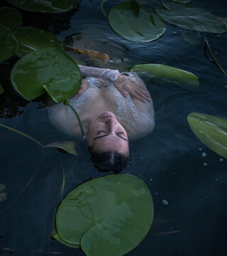 Mystical Slavic mermaid floating in deep lake water among green water lilies, pagan nymph undine in white lace dress, dark fairytale and mythology concept
