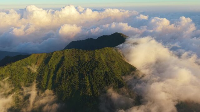 Aerial view of the lush green slopes of the Sindoro Sumbing mountains emerging above a sea of clouds at sunrise in Kecamatan Kedu, Jawa Tengah, Indonesia.