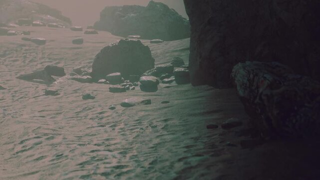 A rocky landscape is visible by the shore as light fog settles over the area. The sun is just starting to rise, creating a soft glow around the stones.