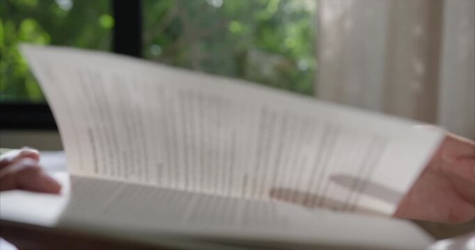 Close up. Hand Asian Woman reading Book on Table  in Cozy Living Room, Warm Morning Sunlight, Slow Living Routine