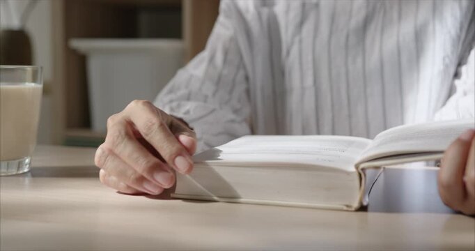 Close up. Hand Asian Woman reading Book on Table in Cozy Living Room, Warm Morning Sunlight