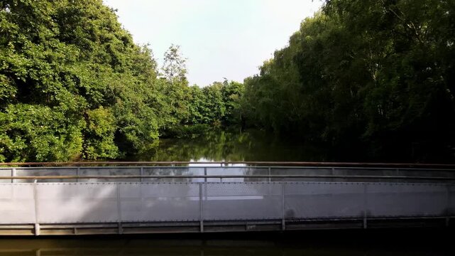 Aerial view of a pedestrian bridge crossing a calm canal surrounded by lush green trees in Delft, South Holland, Netherlands.