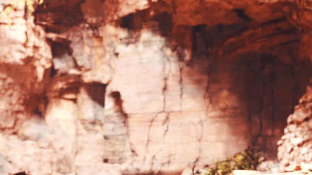 People are exploring a rocky area that has unique shapes and colors. The sun is shining, creating shadows on the rocks. Plants are visible near the ground.